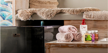 Ein bequemer, weißer Sessel mit Kissen steht vor einer blau gemusterten Wand. Darunter befindet sich ein Fußbad mit Handtüchern und Pflegeprodukten, bereit für eine entspannende Fußpflegebehandlung bei Nina's Studios.